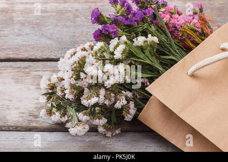 White, purple, pink statice limonium flowers in paper bag. Close up. Old wooden table background. Stock Photo