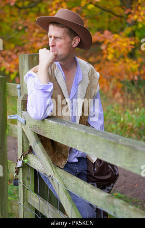 A man leans against a fence post whistling Stock Photo