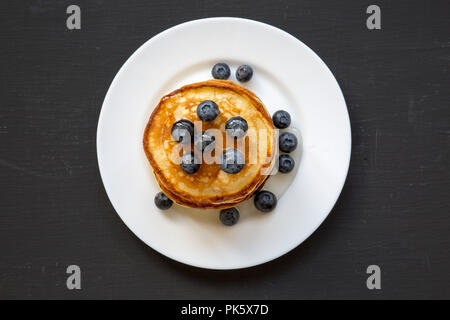 Pancakes with blueberries and honey on white plate on dark wooden background, top view. Flat lay, overhead, from above. Stock Photo