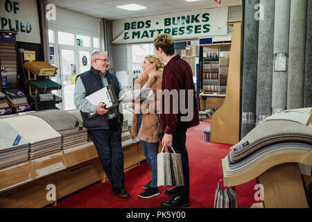 Young couple are discussing design ideas with a senior sales clerk in a carpet shop. Stock Photo