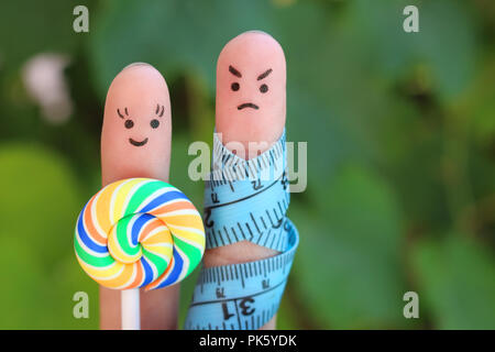 Finger art of couple with meter and candy. Concept of man angry because woman wants to lose weight. Stock Photo