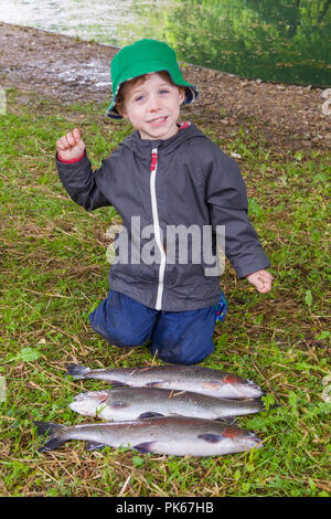 Four year old boy with his three large rainbow trout fish, Meon Springs Trout fishery, East Meon, Hampshire, England, United Kingdom. Stock Photo