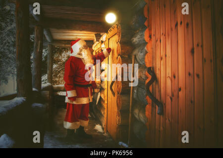 The real Santa Claus knocks on the door of the hut in the winter forest. Stock Photo