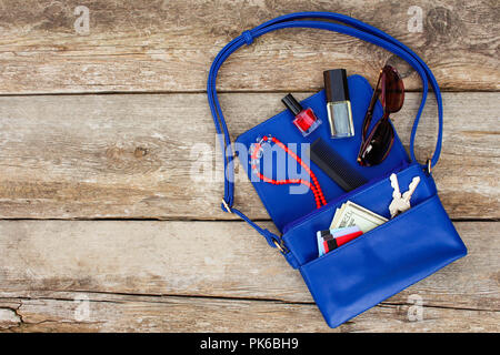 Things from open lady purse. Cosmetics, money and women's accessories fell out of blue handbag. Top view. Stock Photo