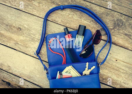 Things from open lady purse. Cosmetics, money and women's accessories fell out of blue handbag. Top view. Toned image. Stock Photo