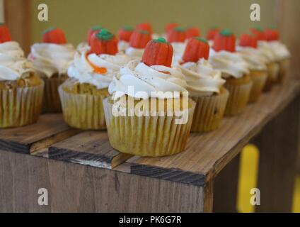 yellow cupcakes with white icing and orange candy on top sitting on a wooden table Stock Photo