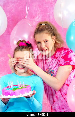 Two beautiful young preteen girls celebrating at a birthday party.  Pink and Aqua balloons and decorations including cake.  Gifts and girls having fun Stock Photo