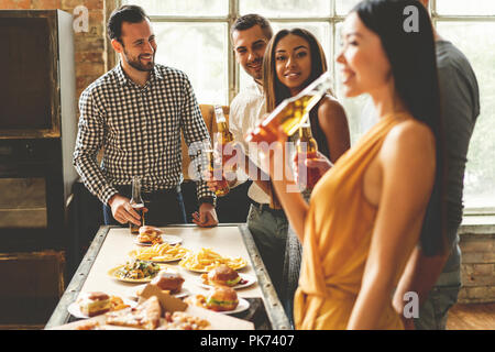 Home party. Full length of cheerful young people enjoying home party while communicating and eating snacks on the kitchen. Stock Photo