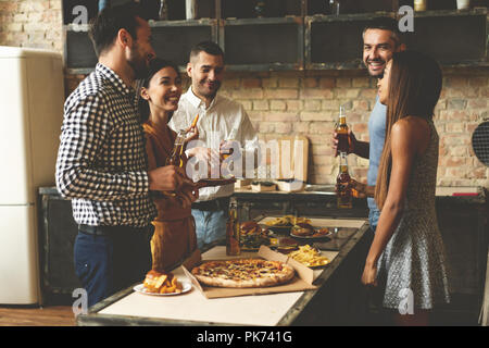 Home party. Full length of cheerful young people enjoying home party while communicating and eating snacks on the kitchen. Stock Photo