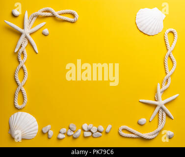 Summer time concept with starfish, shells, stones and rope on a plain yellow background Stock Photo