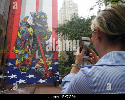 New York, USA. 11th Sep, 2018. A woman photographs the mural 'The Braves of 9/11' by Brazilian artist Eduardo Kobra. 17 years after the terrorist attacks of September 11, 2001, an artist in New York unveiled his mural of a grieving firefighter. Credit: Johannes Schmitt-Tegge/dpa/Alamy Live News Stock Photo