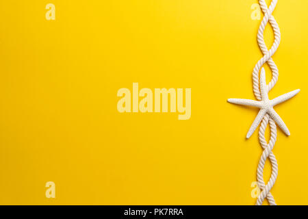 Summer time concept with starfish and rope on a plain yellow background Stock Photo