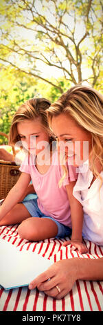 Mother and daughter reading book while father and son playing with football in park Stock Photo