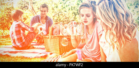 Mother and daughter blowing bubble while father and son playing with football in park Stock Photo