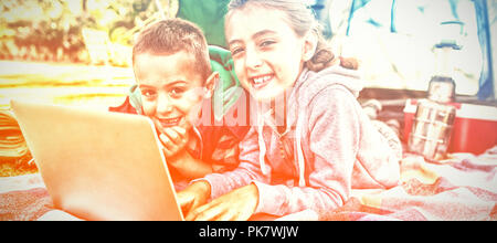 Siblings using laptop outside the tent at campsite Stock Photo