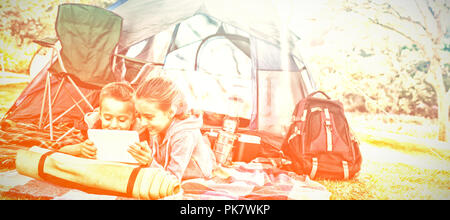 Siblings using laptop outside the tent at campsite Stock Photo