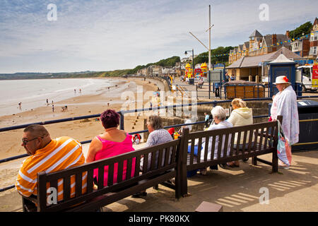 UK, England, Yorkshire, Filey, visitors sat on benches above beach and Coble Landing in sunshine Stock Photo