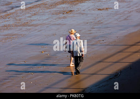 UK, England, Yorkshire, Filey, senior couple walking on beach at low tide in sunshine Stock Photo