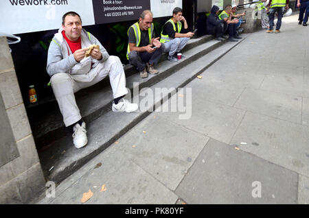 Construction workers eating and checking their phone during a break - London, England, UK. Stock Photo