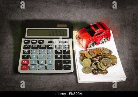 Car loan concept, a calculator beside the red toy car and coins on a spiral notebook. Stock Photo