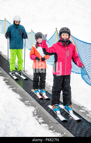 Two girls with father going up to the slope on the carpet ski lift. Stock Photo