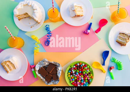 Cake, candy, chocolate, whistles, streamers, balloons, juice on holiday table. Concept of children's birthday party. View top. Stock Photo