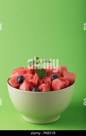 Sliced ​​slices of watermelon with blueberries in a plate on a green background. Food with space for text Stock Photo