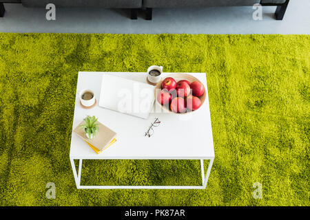 elevated view of table with laptop, coffee cups, apples in bowl, books, eyeglasses and plant at home Stock Photo