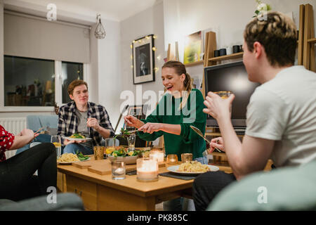 Two young couples are having a dinner party and one woman is laughing while serving salad. Stock Photo