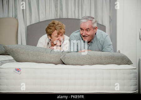 Senior couple are lying on a bed while shopping in a furniture shop. Stock Photo