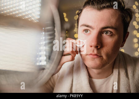 Young man is toning his face during his skin care routine at home. Stock Photo