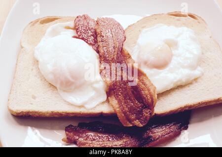 Poached eggs with crispy streaky bacon on white unbuttered toast Stock Photo