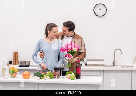 happy adult man presenting tulips bouquet for wife while she cooking Stock Photo