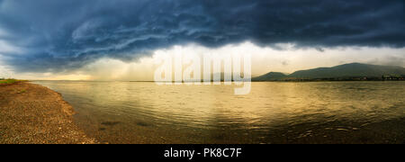 A panorama og golden evening light and a dramatic summer storm reflected in the lagoon at Carleton in Gaspesie, Quebec, Canada Stock Photo