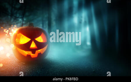 A Spooky Halloween pumpkin Jack O lantern grinning on a misty and dark evening with a misty forest in the background. Stock Photo