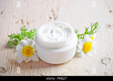 container with cream and chamomiles on wooden background Stock Photo