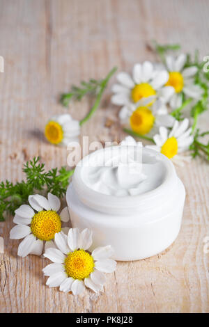 container with cream and chamomiles on wooden background Stock Photo