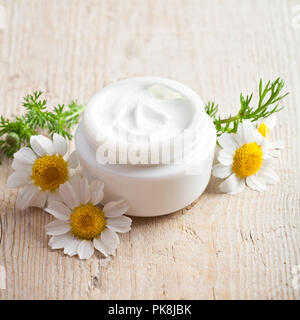 container with cream and chamomiles on wooden background Stock Photo