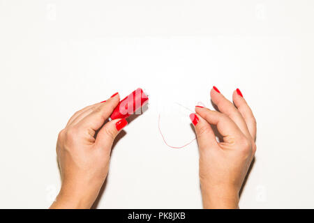 Female hand seamstress, needlewoman holding in hands red thread and needle, background view from above Stock Photo