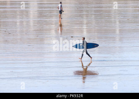 A surfer carrying his surfboard and running across Fistral Beach in Newquay Cornwall. Stock Photo