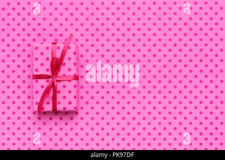 Pink gift box on wrapping paper with polka dots. Minimal background or greeting card with space for text. Holidays concept. Stock Photo