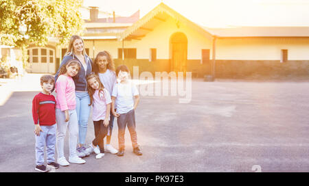 Happy group of children in elementary school is standing with the teacher in the schoolyard Stock Photo