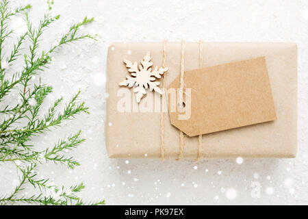 Christmas gift wrapped in kraft paper with empty tag. Glowing snow bokeh, coniferous branch on white. Winter holidays mock up. Stock Photo