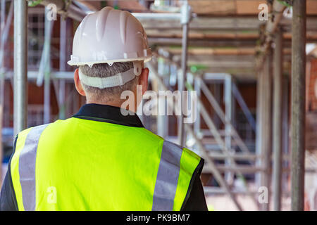 Rear view of male builder construction worker on building site wearing hard hat and hi-vis vest Stock Photo