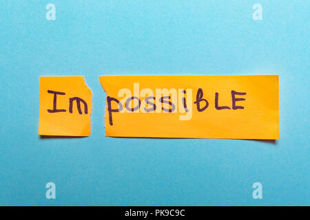 The word impossible is written on yellow paper and torn on a blue background.success and challenge concept,motivation, achievement, goal Stock Photo