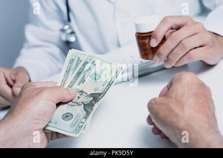 closeup of a caucasian doctor man, in a white coat, giving a bottle of pills to a senior caucasian patient man, who is giving to the doctor some dolla Stock Photo