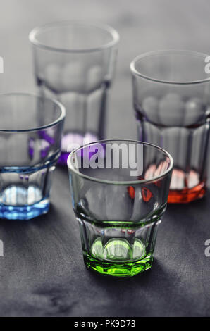 set of transparent glasses of different colors, on a dark wooden table Stock Photo