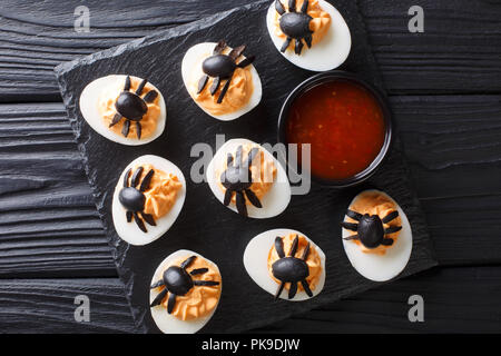 Halves deviled eggs decorated with olive spiders close-up served with ketchup on a black table. Halloween food. horizontal top view from above Stock Photo