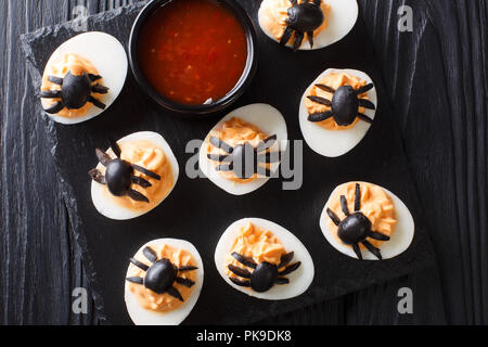 Halloween appetizer deviled eggs stuffed with mustard and decorated with olive spiders and cobweb close-up on a blackboard. horizontal top view from a Stock Photo