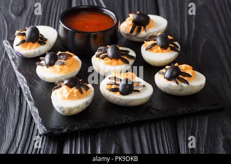 Delicious Halloween appetizer: deviled eggs decorated with olive spiders close-up served with ketchup on a black table. horizontal Stock Photo